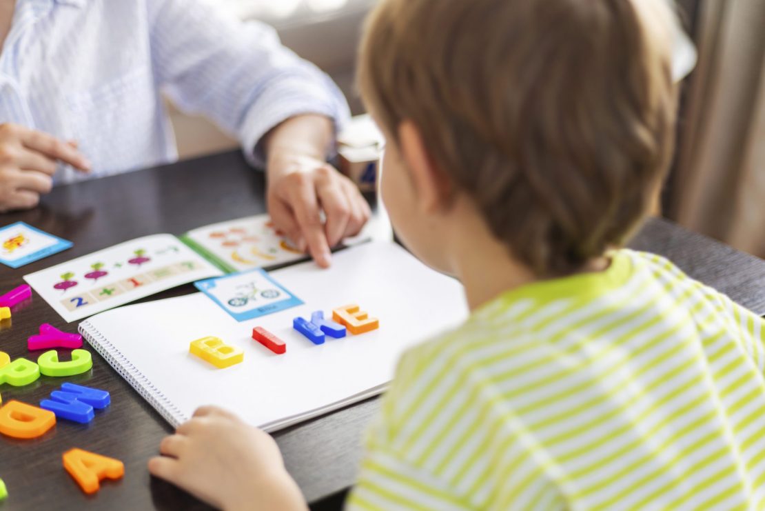 A reading specialist guiding a child through a multi-sensory literacy activity using letter tiles.