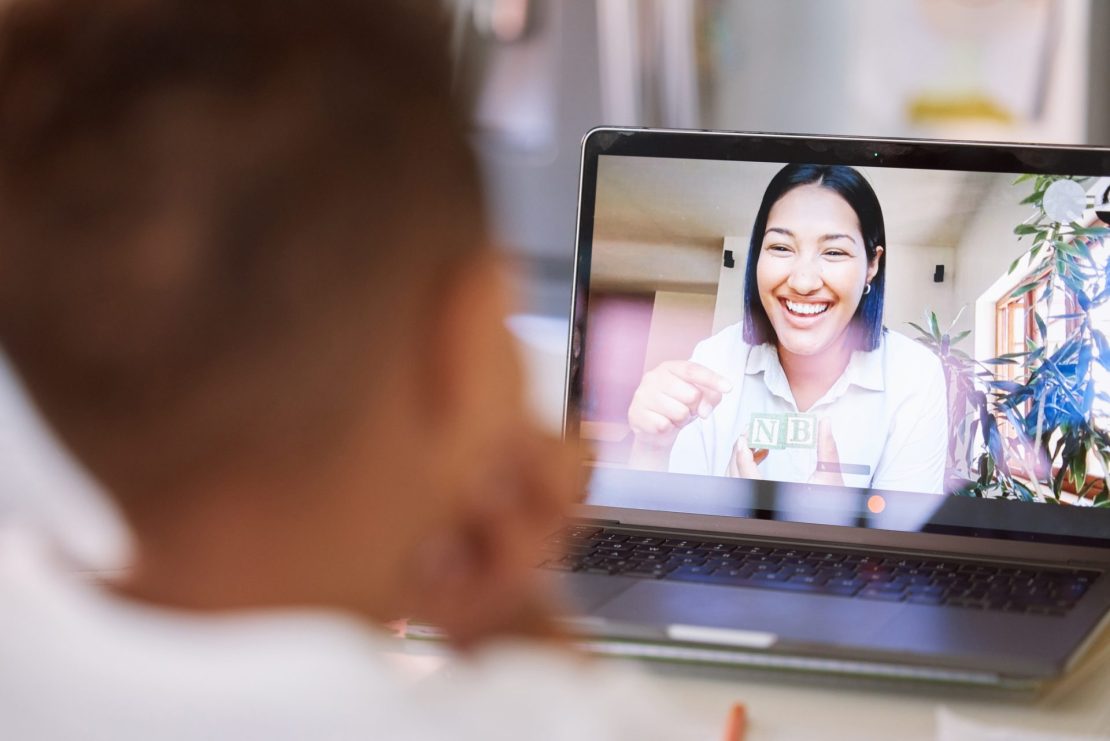 A child receiving online tutoring at home with a laptop and tutor on screen.