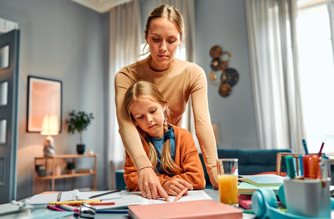 A parent helping a child use a planner and checklist at a desk, illustrating executive functioning skills like organization and time management.
