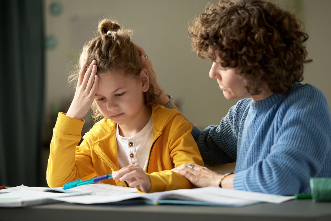 A parent helping a frustrated student with homework at a desk, illustrating signs that a child may be struggling in school and need academic support.